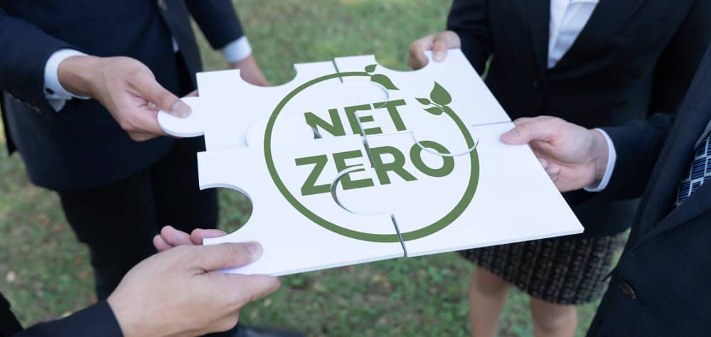 Zdjęcie przedstawia puzle z napisem Net Zero, które trzymają trzy osoby.