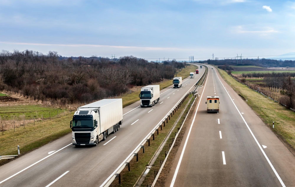 Grafika przedstawia ciężarówki jadące po drodze szybkiego ruchu, będące symbolem emisji z transportu drogowego i budownictwa